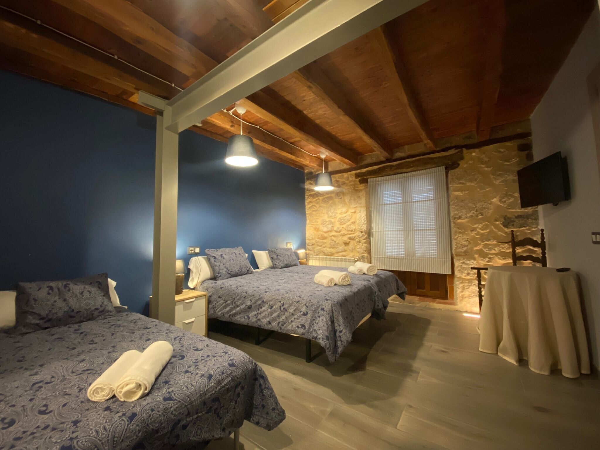 Ein Schlafzimmer mit zwei Betten, einer Steinwand, einem Fernseher und einer Holzbalkendecke.