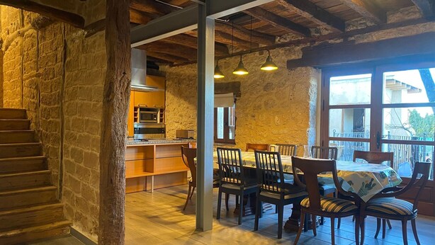 Een rustiek interieur met een houten wenteltrap, stenen muren, een keukenhoek en een eethoek met stoelen en een tafel.