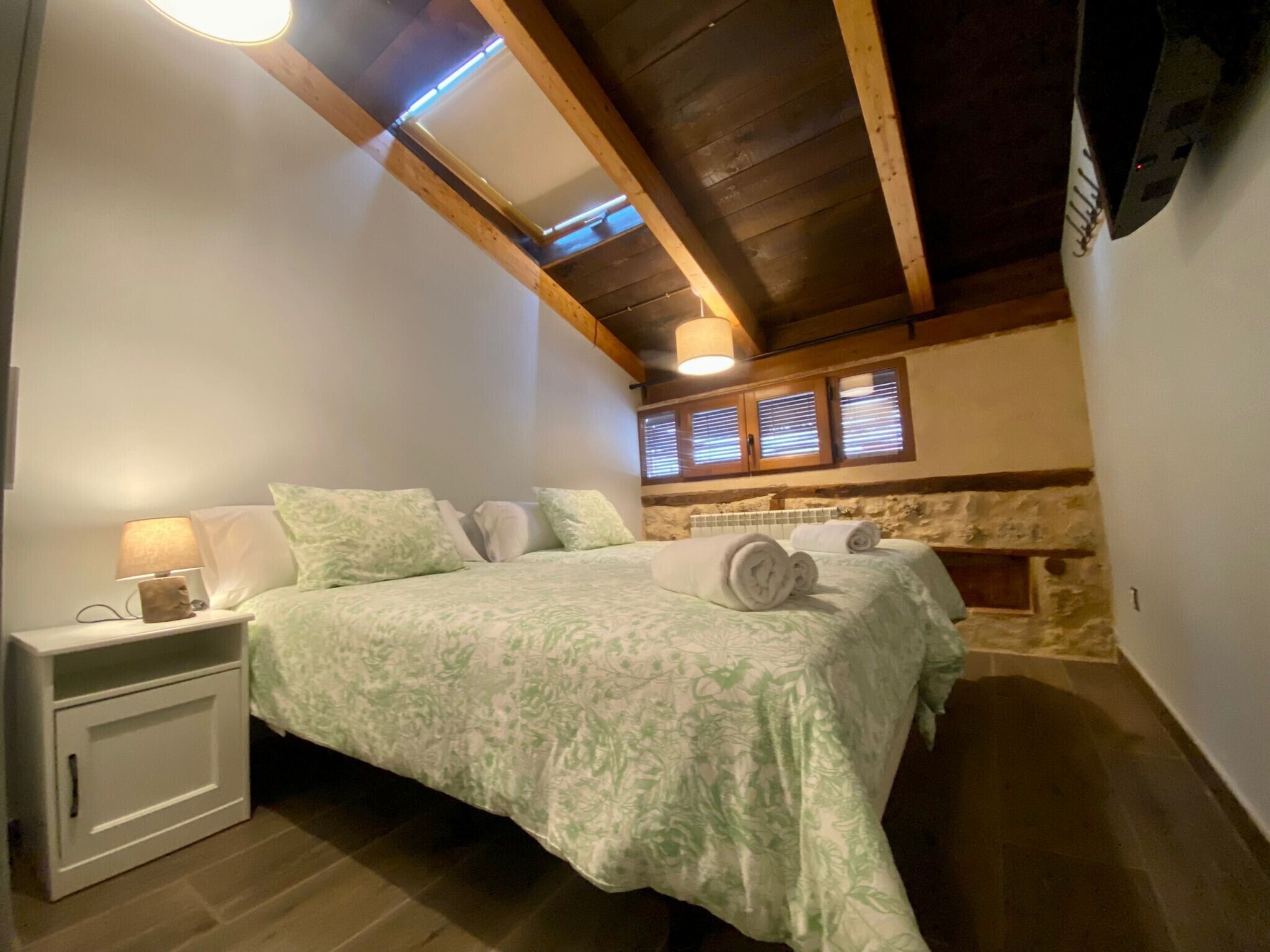 Un dormitorio con cama, mesita de noche, lámpara y pared de piedra.