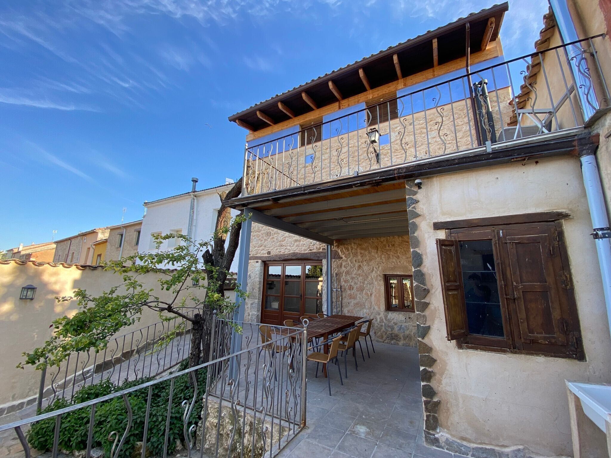 A two-story building with a balcony, stone walls, and a dining area with outdoor furniture.