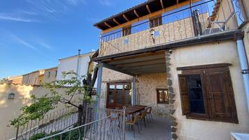 A two-story building with a balcony, stone walls, and a dining area with outdoor furniture.