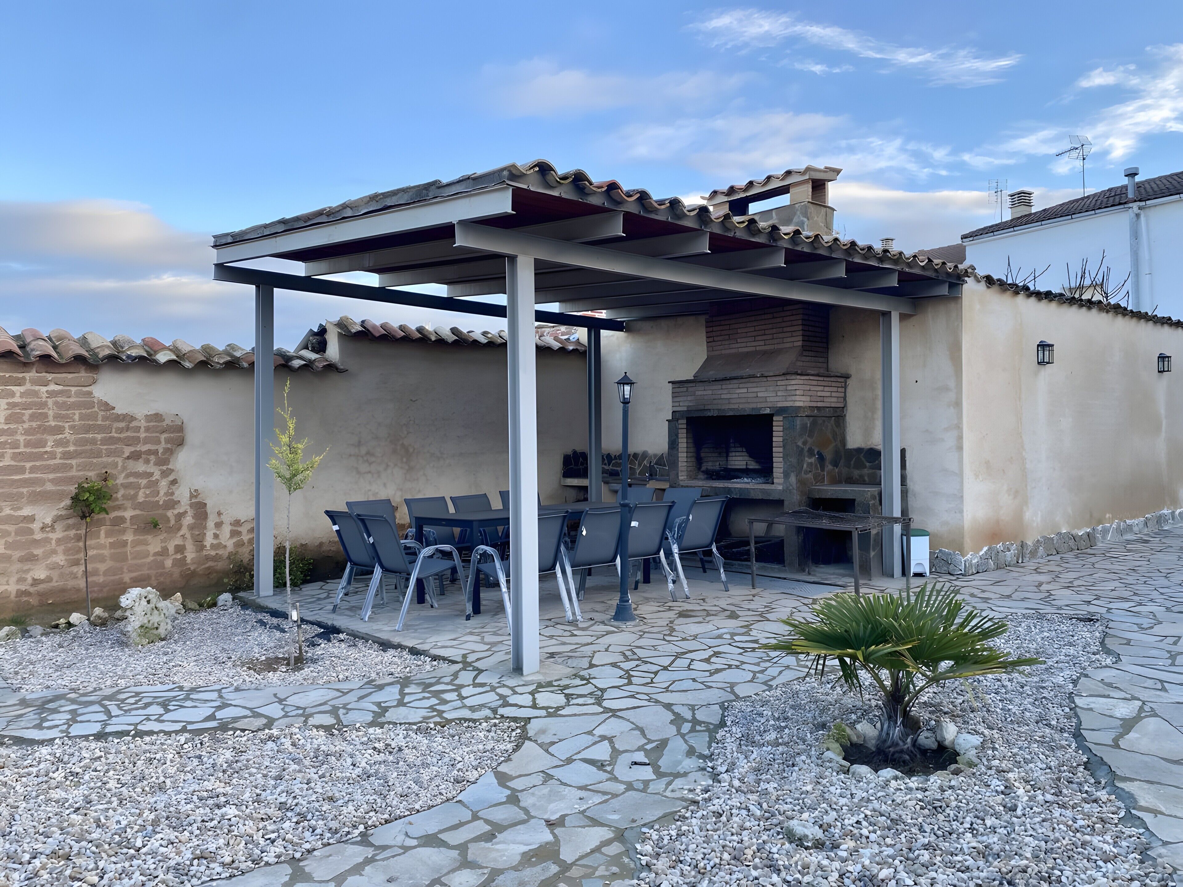 Terrassa exterior amb una pèrgola, paviment de pedra i un forn de lladrics.