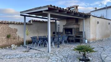 Terrassa exterior amb una pèrgola, paviment de pedra i un forn de lladrics.