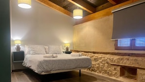 Een slaapkamer met een bed, bedlampen, een stenen muur en een raam met zonwering.