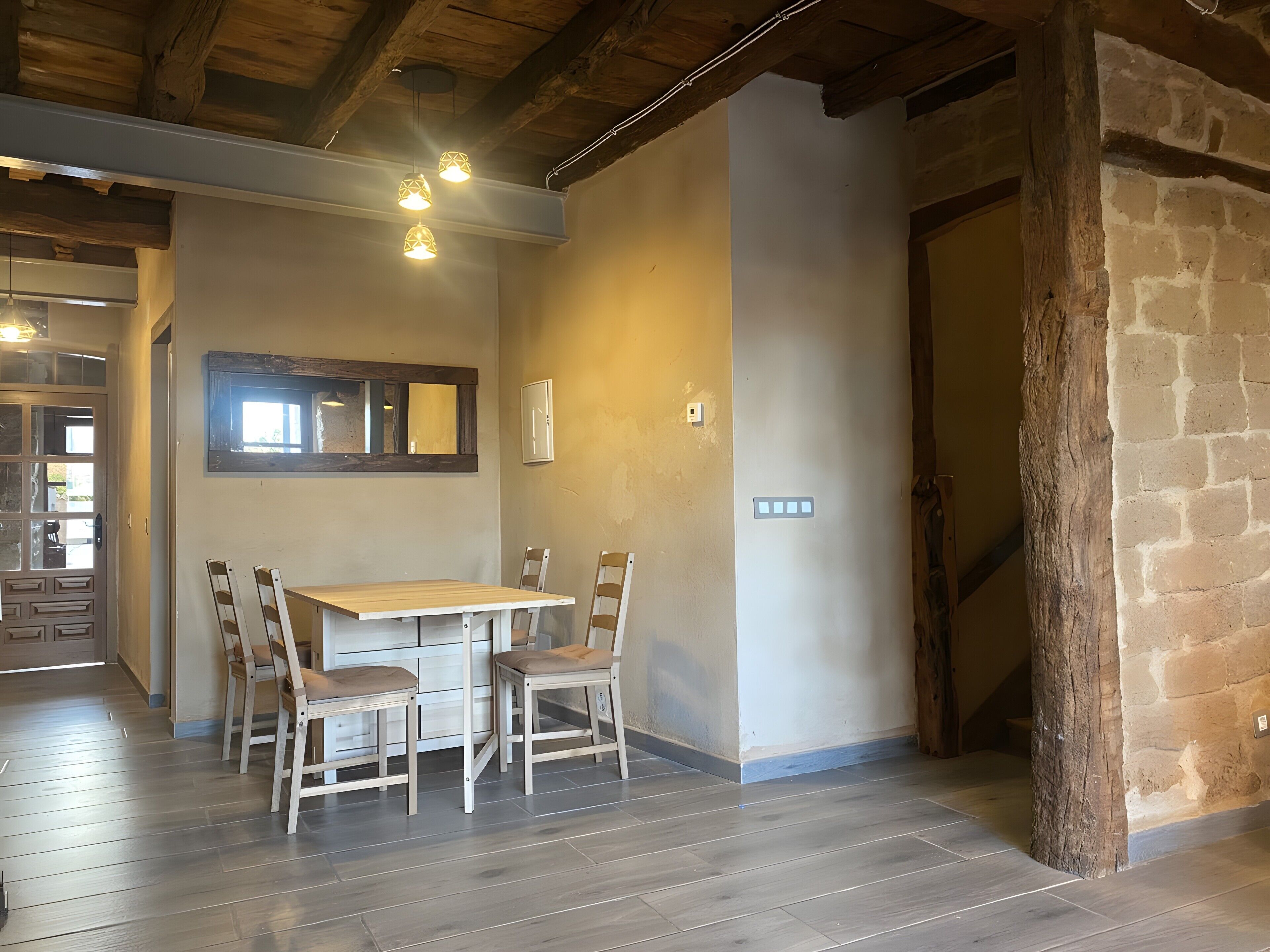 A dining area with a wooden table and chairs, a window with a mirror, and a stone wall.