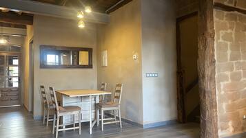 A dining area with a wooden table and chairs, a window with a mirror, and a stone wall.