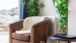 Un sillón de cuero marrón con una manta blanca, una mesita redonda con un objeto negro encima y una cesta tejida en el suelo.