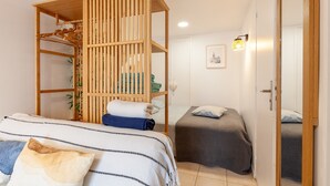 Una habitación con una cama litera, una mesita de noche pequeña, una lámpara de noche y una puerta que da a otra habitación.