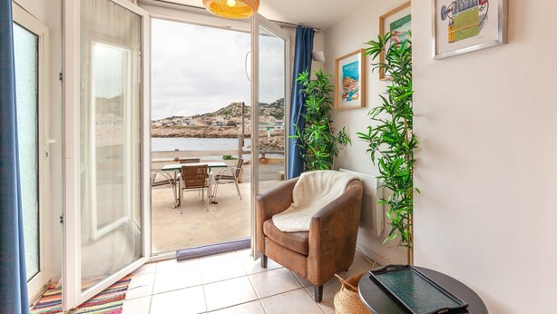 Una habitación con puerta de vidrio corrediza que da a un espacio al aire libre, un sillón marrón, una lámpara de fibra y un cuadro de Marsella.