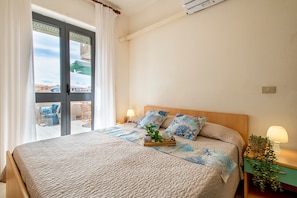 A hotel room with a bed, a bedside table with a lamp, a window with curtains, and a view of the outside.
