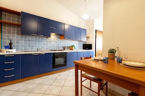A modern kitchen with blue cabinets, a wooden dining table, and a tiled backsplash.