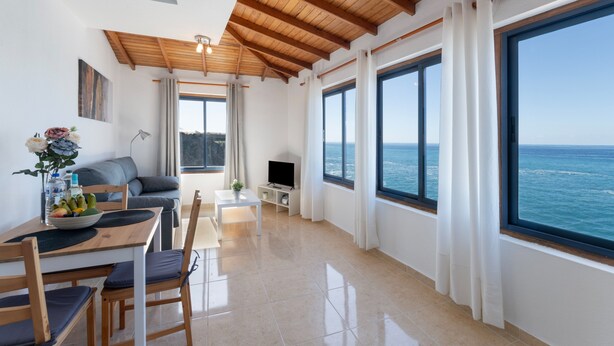 Una sala de estar moderna con comedor, ventanas amplias y vista al mar.