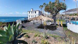 A coastal property with a pool, outdoor seating, and a view of the ocean.