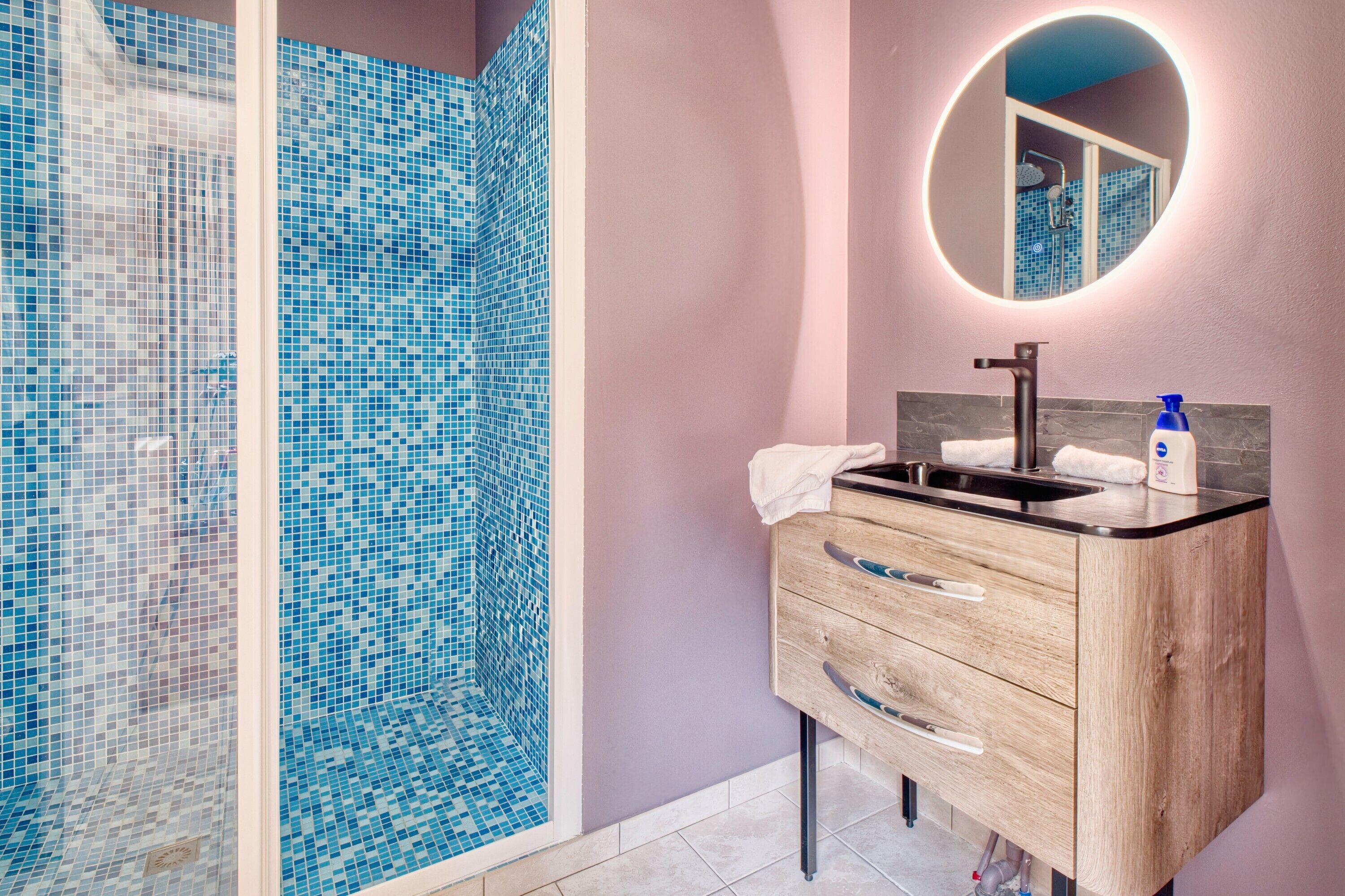A bathroom with a shower, a sink, a mirror, and a wooden cabinet.