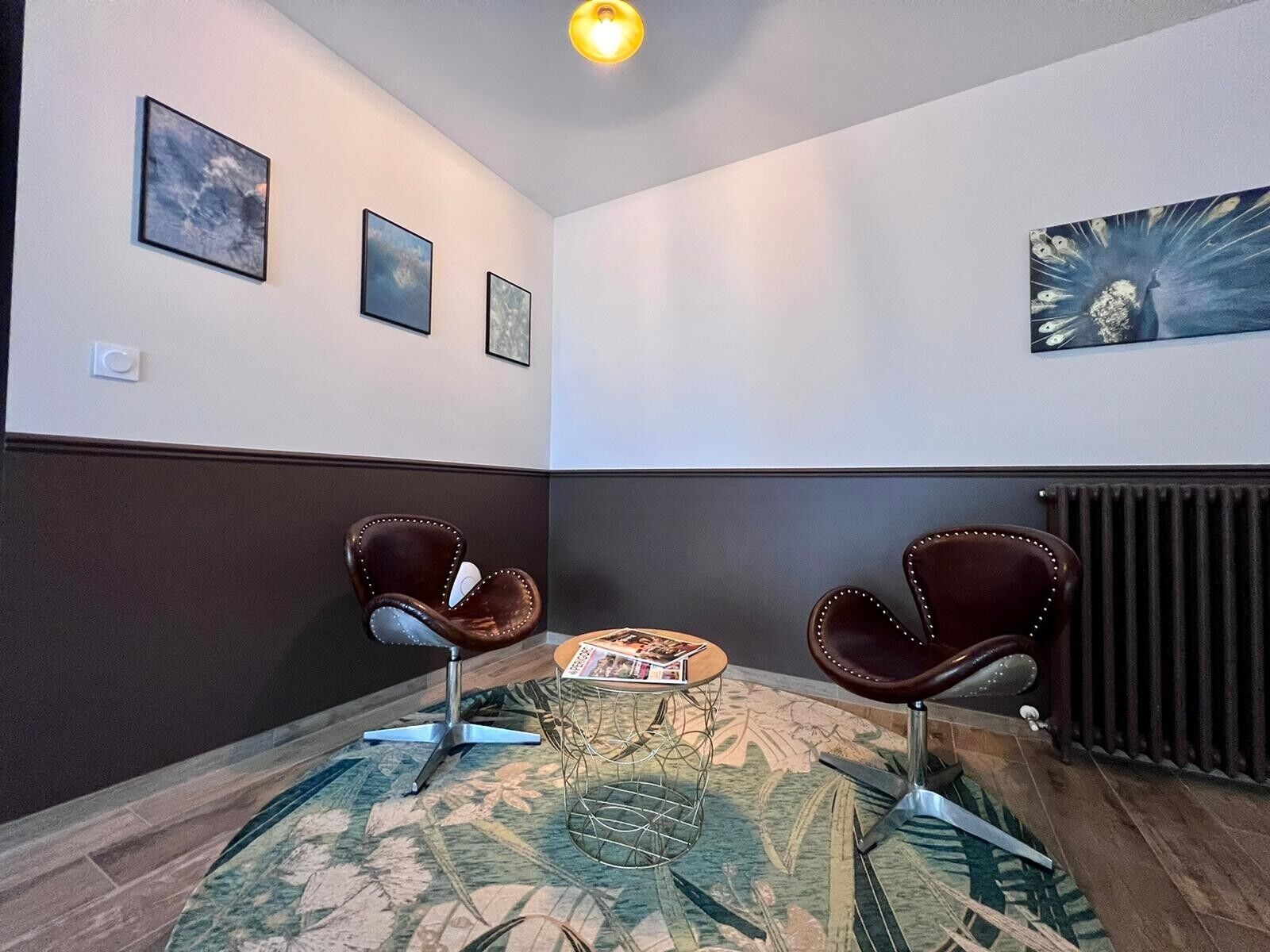 Ein Zimmer mit zwei Ledersesseln, einem kleinen runden Tisch, einer Zeitschrift und einem Heizkörper.