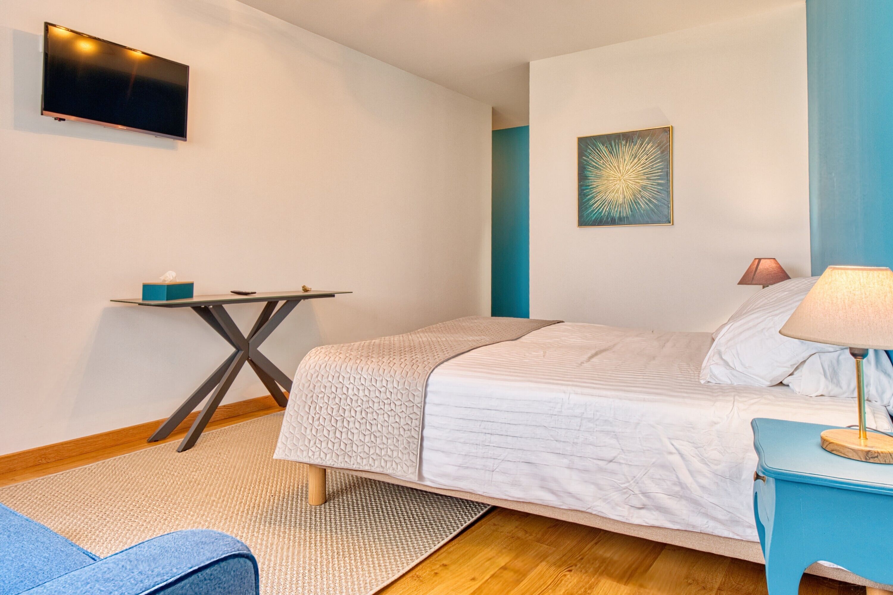 A bedroom with a bed, a desk, a TV, and a lamp.