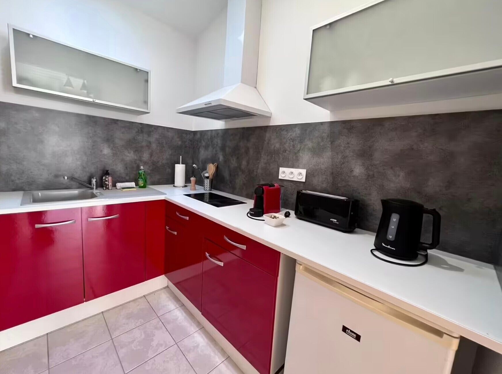 A kitchen with red cabinets, a white countertop, a black toaster, a coffee maker, and a sink.