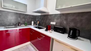 A kitchen with red cabinets, a white countertop, a black toaster, a coffee maker, and a sink.