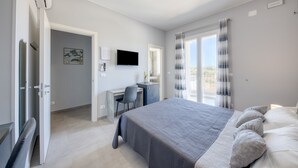 Ein Schlafzimmer mit Bett, Schreibtisch, Stuhl, Fernseher und einem Fenster mit Vorhängen.