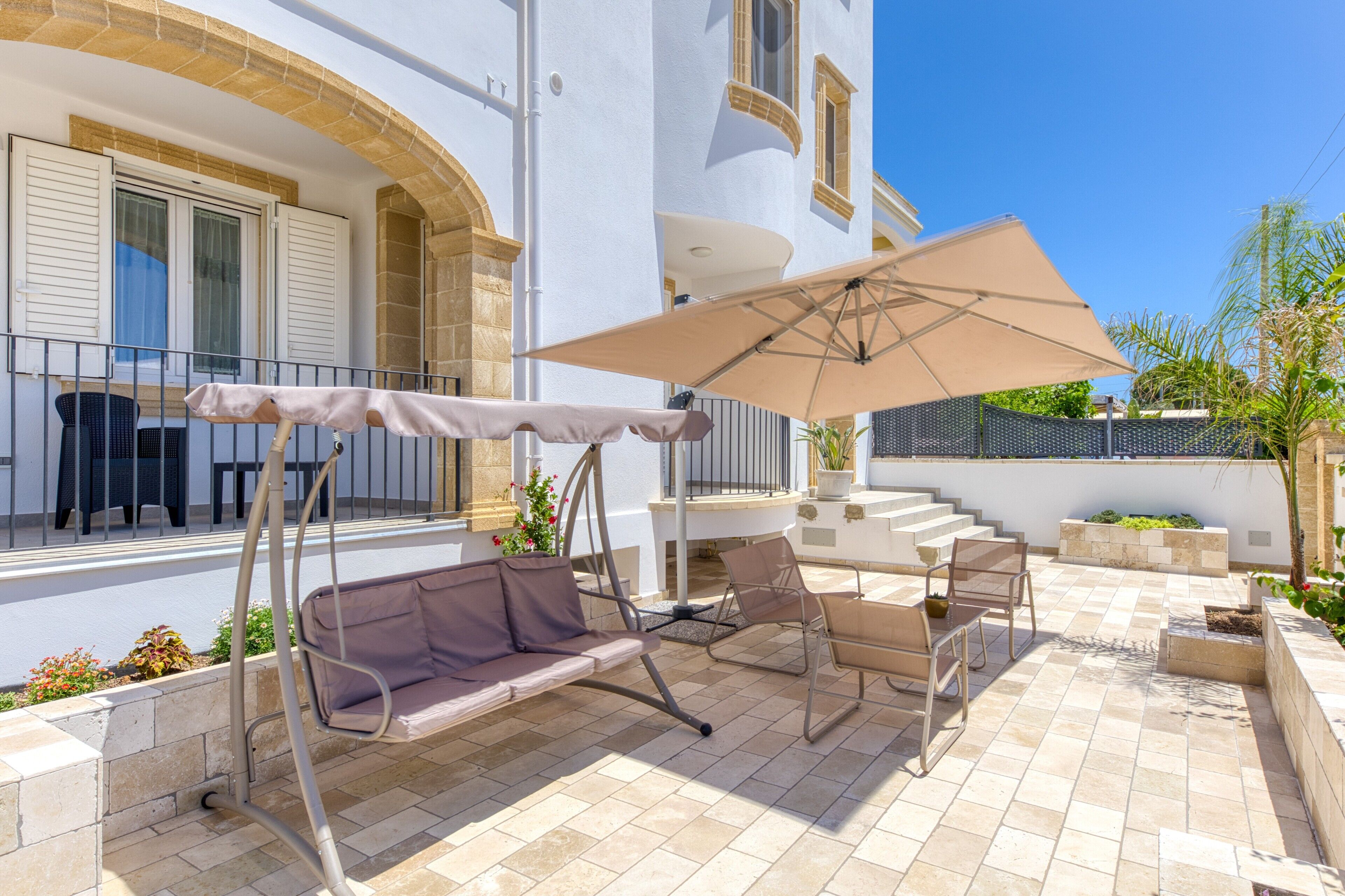 A patio with a swing chair, a table with an umbrella, and a staircase leading to an upper level.