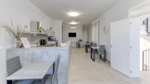 Una cocina moderna con encimera de mármol, horno integrado y televisor de pantalla plana. Hay un comedor con mesa y sillas, y una escalera que lleva a un nivel superior.