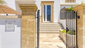 Entrada de una villa con un pilar de piedra, una puerta metálica y un letrero con el nombre de la villa.