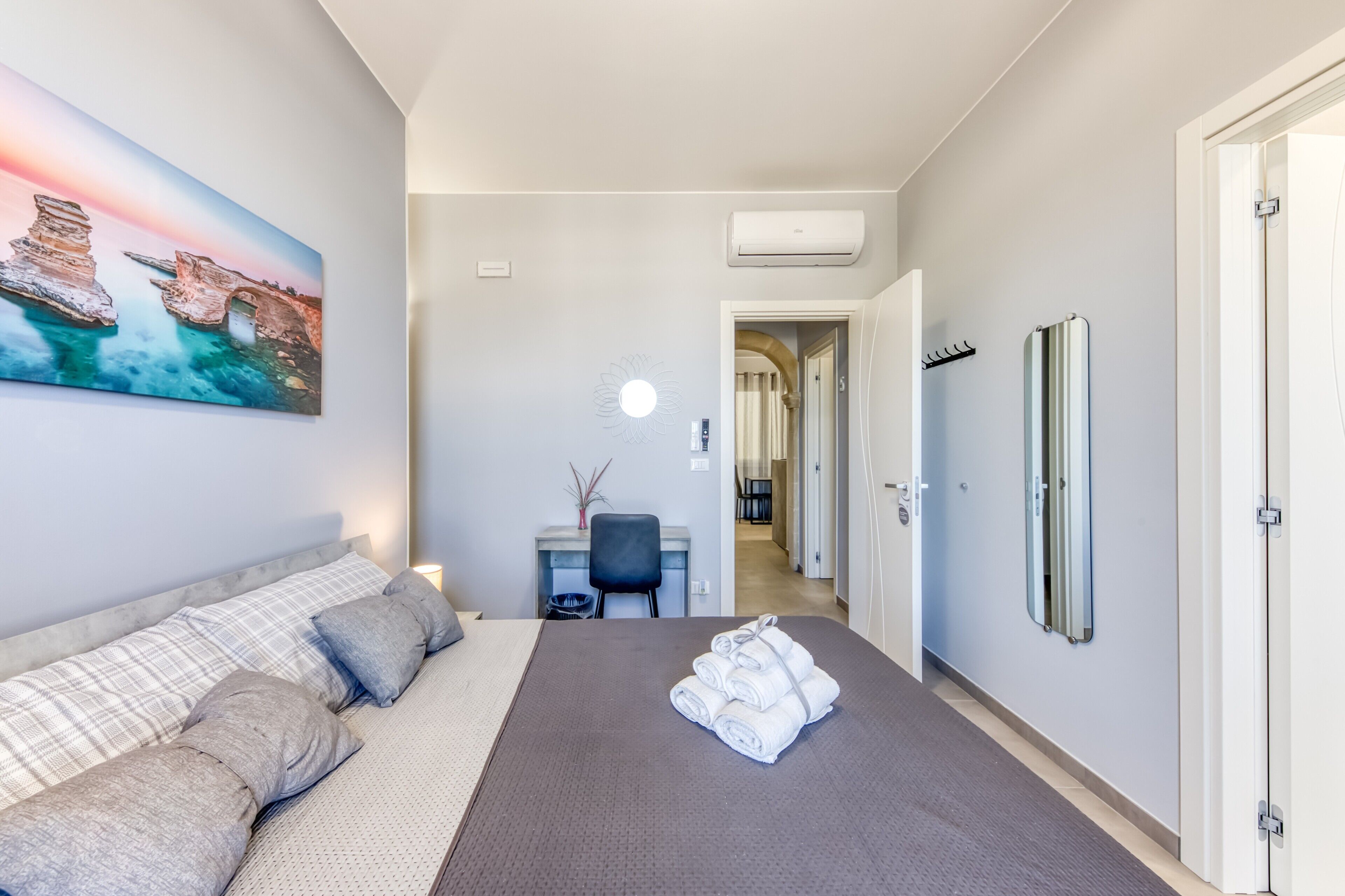 A hotel room with a bed, a desk, a chair, a painting, and a bathroom door.