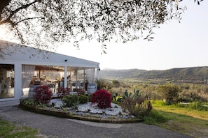 Una casa con un portico coperto, un giardino pieno di piante varie e vista sulla campagna.