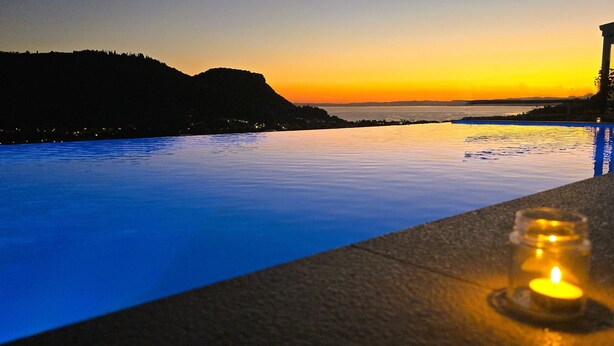 Una piscina con vista sul tramonto, una candela sul bordo e un edificio sullo sfondo.