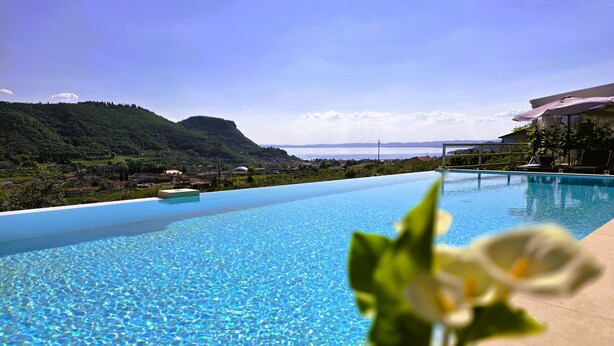 Una piscina infinita de color azul intenso con vistas a un paisaje montañoso y una masa de agua en la distancia.