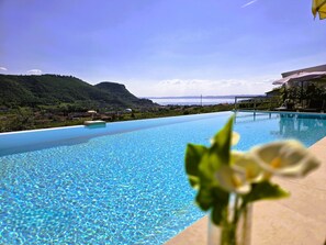 A clear blue infinity pool with a view of a mountainous landscape and a body of water in the distance.