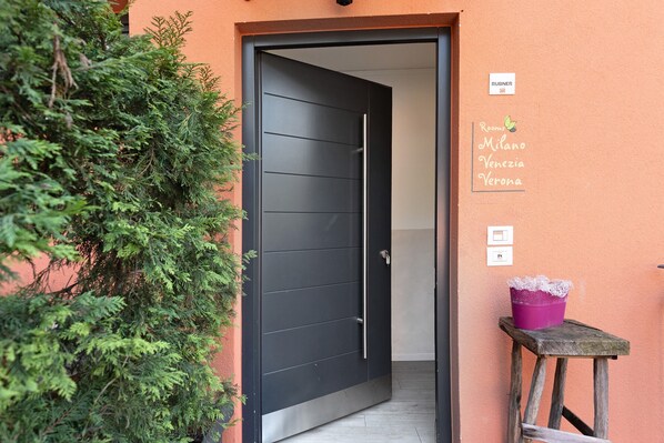 A black door with a handle, a small wooden stool with a purple bucket, and a sign with room names.
