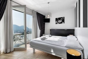 A bedroom with a bed, a TV, a picture on the wall, and a balcony with a view.