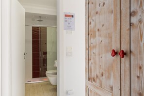 A bathroom with a glass shower enclosure, a toilet, and a wooden wardrobe with red handles.