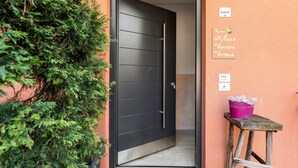 Een deur met een bord waarop 'Kamers Milaan Venetië Verona' staat, en een klein tafeltje met een paarse emmer ernaast.