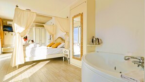 Een slaapkamer met een hemelbed, een groot wit bad en een spiegel met gouden lijst.