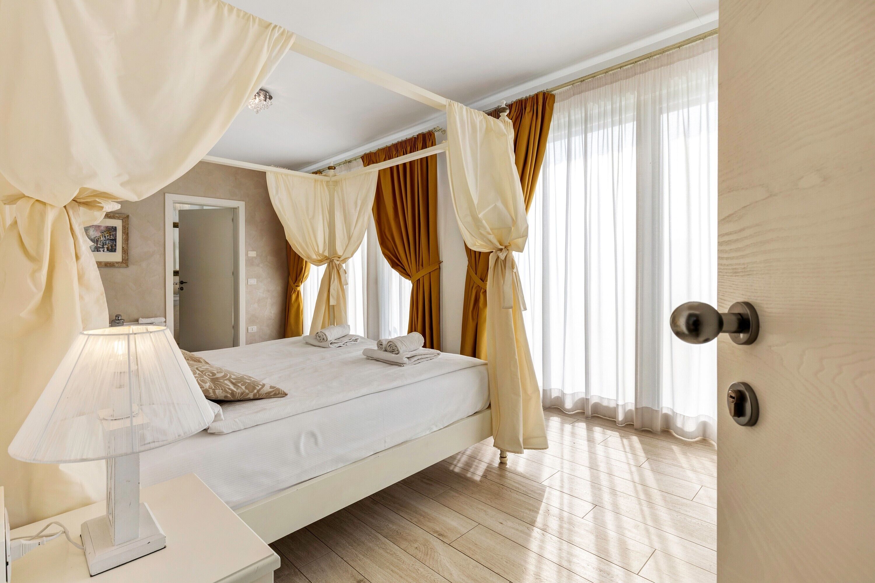 Une chambre à coucher avec un lit, une table de chevet, une lampe, des rideaux et une porte.