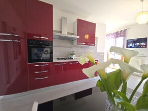 Eine moderne Küche mit roten Schränken, einem eingebauten Ofen und einem Gasherd. Auf der Arbeitsfläche steht ein Blumentopf mit weißen Blüten.