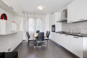 Een moderne keuken met witte kastjes, een eettafel met stoelen, een fornuis en een raam met gordijnen.