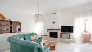 Uma sala de estar com um sofá verde-água, uma mesa de centro de madeira, uma lareira e uma televisão.