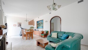 Uma sala de estar com sofá, mesa de centro, mesa de jantar, cadeiras e um quadro na parede.