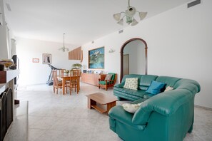 Una sala de estar con sofá, mesa de centro, mesa de comedor, sillas y un cuadro en la pared.