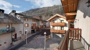 Ein traditionelles Steinhaus mit einem Holzbalkon, einem gepflasterten Innenhof und einer Bergkulisse.
