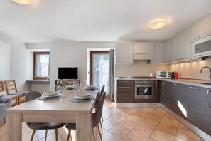 A modern kitchen with stainless steel appliances, a dining area with a wooden table, and a TV in the living room.