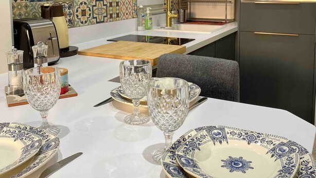 Een moderne keuken met een inbouwoven, een betegelde spatwand en een eethoek met borden en glazen.