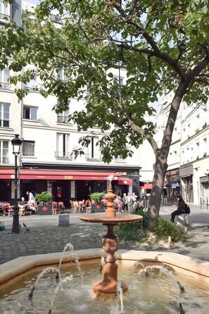 A public square with a fountain, outdoor seating, and a building with a red awning.