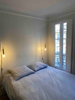A bedroom with a bed, two bedside lamps, and a window with a balcony view.