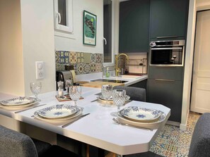 A modern kitchen with a dining table set for four, a built-in oven, and a backsplash with colorful tiles.