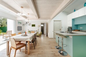 A modern kitchen with a bar area, wooden flooring, and a dining area with a table and chairs. - Architect's Villa 800m from the Sea – Comfort, Nature, and Serenity in Oléron, with Terrace Garden (Dolus-d'Oleron)