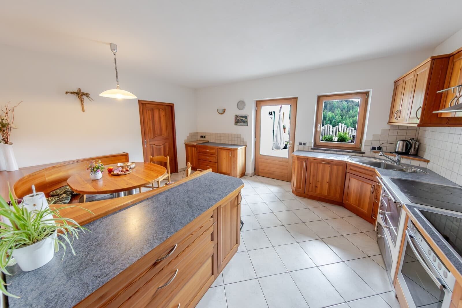 Cucina con zona pranzo, mobili in legno, forno a incasso e finestra con vista sul verde.